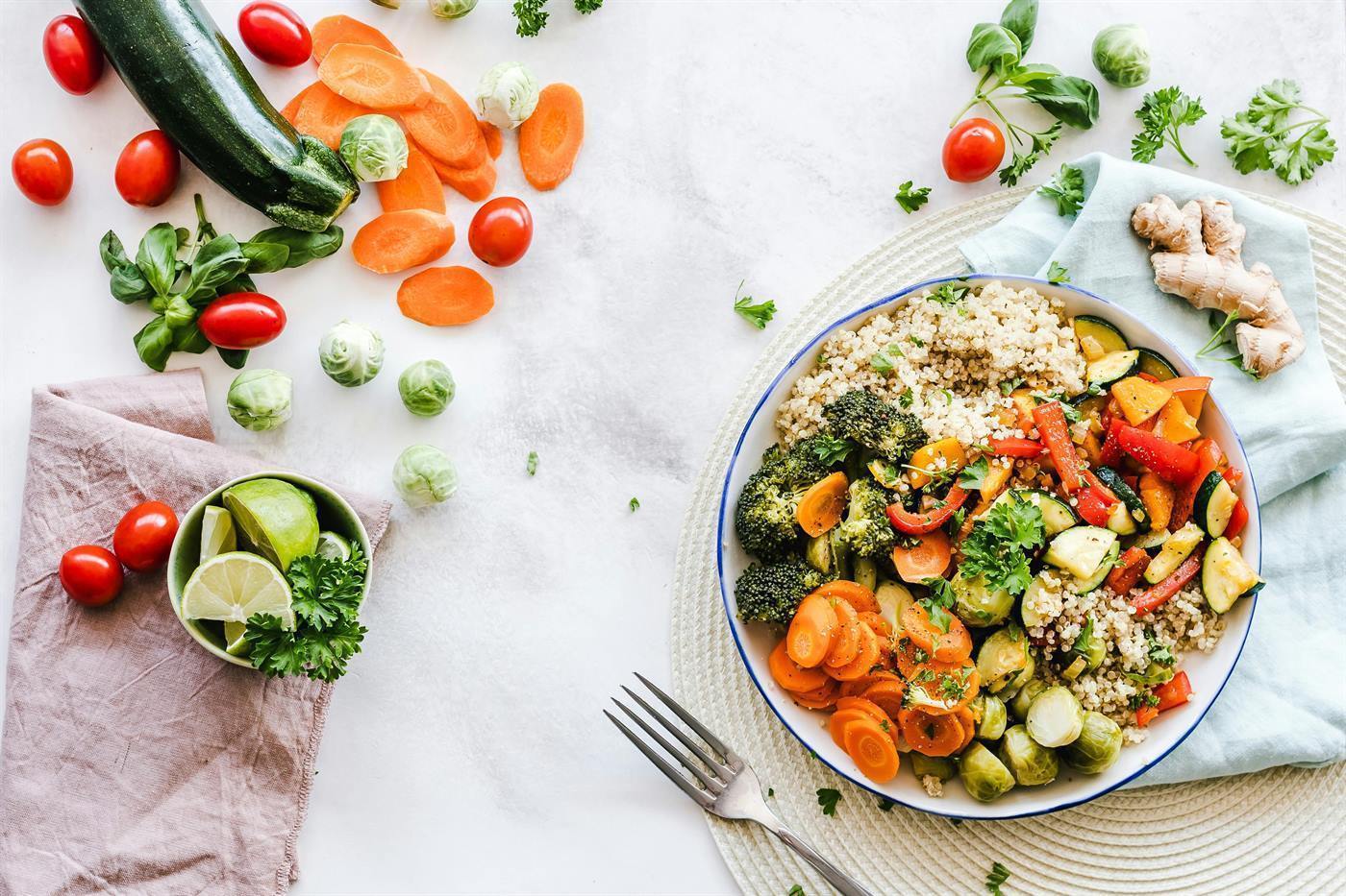 A bowl of quinoa and roasted vegetables surrounded by fresh produce
